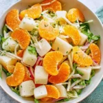 Mexican Jicama and Citrus Salad with orange slices, jicama cubes, and red onion in a white bowl.