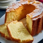 A golden Million Dollar Pound Cake dusted with powdered sugar, sliced and served on a white plate.
