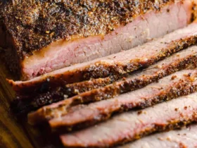 Sliced Oven Baked Texas Beef Brisket with a crispy seasoned bark and juicy pink interior on a wooden cutting board.