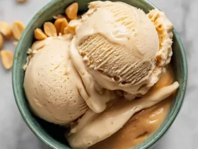 Peanut Butter Banana Ice Cream 44 Two scoops of creamy Peanut Butter Banana Ice Cream in a green bowl with scattered peanuts.