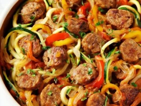 Sausage and Peppers with Zucchini Noodles 47 A bowl of Sausage and Peppers with Zucchini Noodles featuring sliced sausage, colorful bell peppers, and spiralized zucchini in a savory sauce.