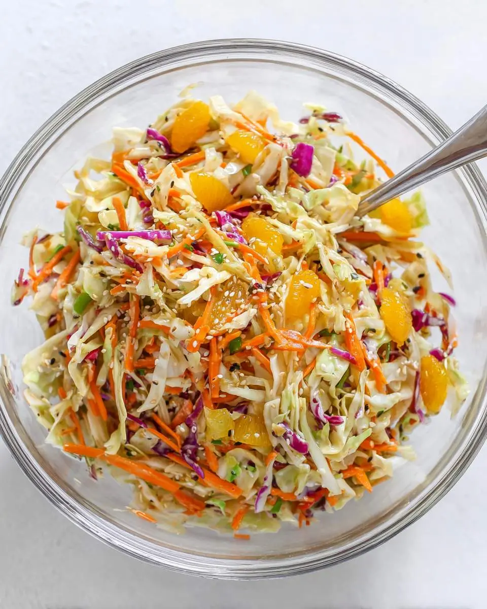 Sesame Orange Napa Cabbage Salad 28 A glass bowl filled with Sesame Orange Napa Cabbage Salad featuring shredded cabbage, carrots, mandarin oranges, and sesame seeds.