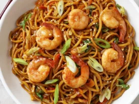 A white bowl filled with Shrimp Lo Mein noodles topped with six cooked shrimp, green onions, and sesame seeds.