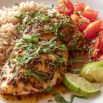 Slow Cooker Mojo Chicken served on a white plate with rice, tomatoes, and lime wedges, topped with fresh cilantro.