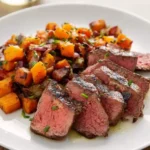 Sliced medium-rare steak with sweet potato hash served on a white plate, garnished with fresh herbs.