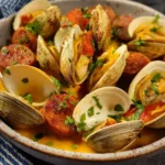 Steamed Clams with Italian Sausage served in a rustic bowl with golden broth and fresh herbs.