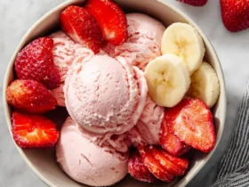 A bowl of creamy Strawberry Banana Ice Cream topped with fresh strawberry slices and banana rounds on a marble surface.