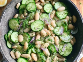 A bowl of White Bean and Cucumber Dill Salad with sliced cucumbers, white beans, red onion, and fresh dill on a wooden table.