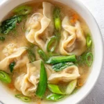 A warm bowl of Wonton Soup with delicate dumplings, fresh green vegetables, and clear broth in a white bowl.