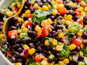 black bean salad with corn 35 Close-up of a colorful black bean salad with corn, tomatoes, cilantro, and red onion in a white bowl with a gold spoon.