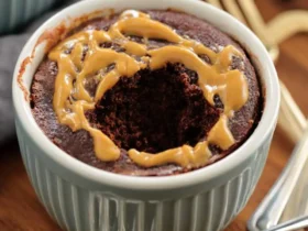 Chocolate Peanut Butter Mug Cake 53 Chocolate Peanut Butter Mug Cake in a blue ramekin with a bite taken out, drizzled with peanut butter on top.