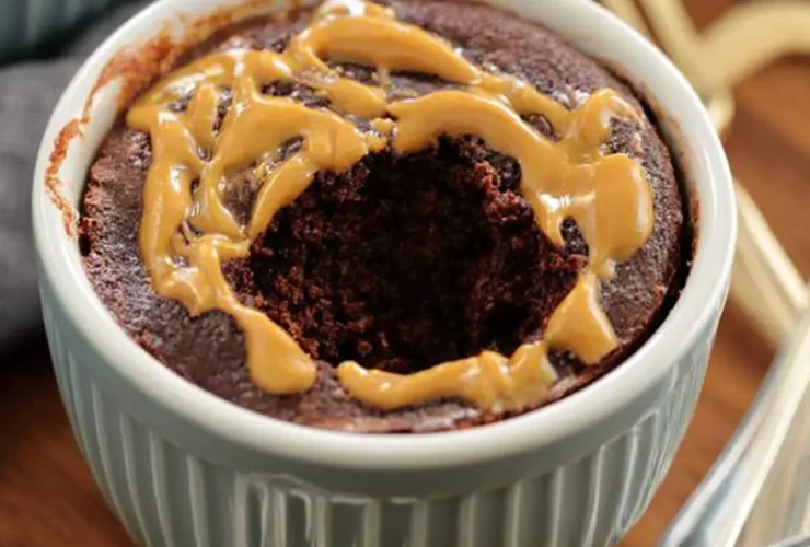 Chocolate Peanut Butter Mug Cake in a blue ramekin with a bite taken out, drizzled with peanut butter on top.