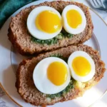 Two slices of meatloaf with eggs on a white plate, each topped with halved soft-boiled eggs revealing bright yellow yolks.