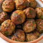 A bowl of golden-brown Moroccan Lamb Meatballs garnished with fresh herbs, perfectly seared and stacked.