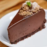 A slice of creamy No Bake Chocolate Cheesecake topped with cookie crumbles and a mint leaf on a white plate.