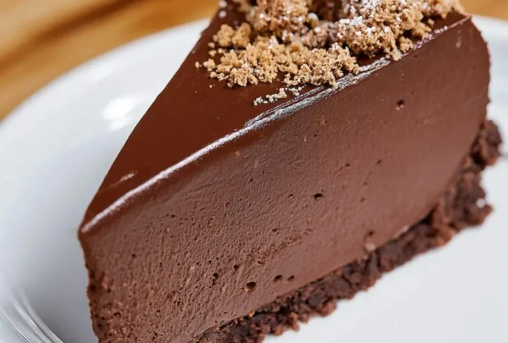 A slice of creamy No Bake Chocolate Cheesecake topped with cookie crumbles and a mint leaf on a white plate.
