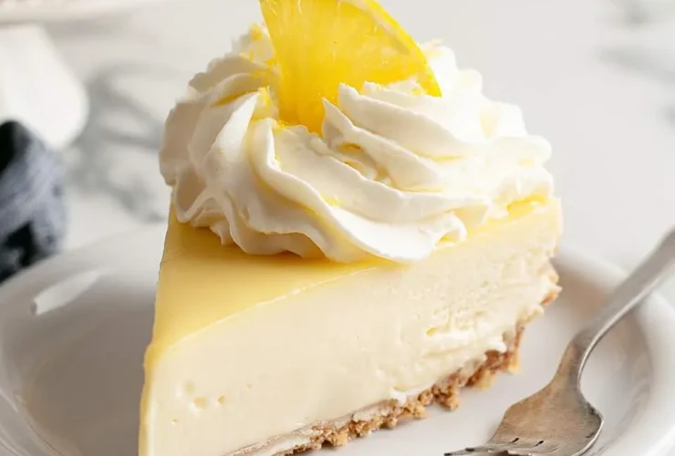 A creamy slice of No-Bake Lemon Cheesecake topped with whipped cream and a lemon slice on a white plate.