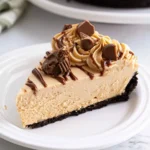 A slice of No Bake Peanut Butter Cheesecake with chocolate drizzle and peanut butter cups on a white plate.
