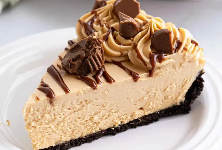 A slice of No Bake Peanut Butter Cheesecake with chocolate drizzle and peanut butter cups on a white plate.