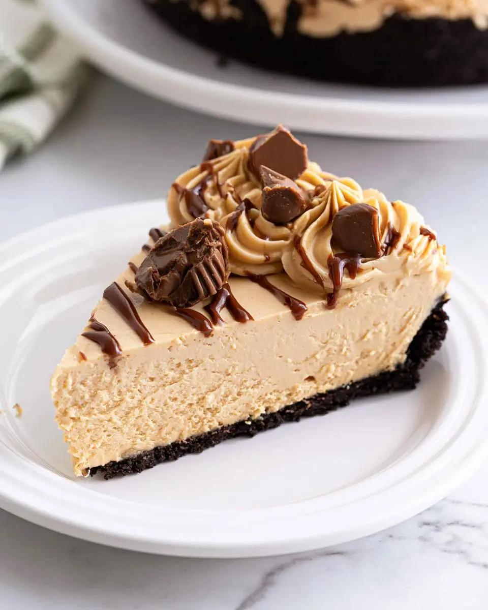 A slice of No Bake Peanut Butter Cheesecake with chocolate drizzle and peanut butter cups on a white plate.