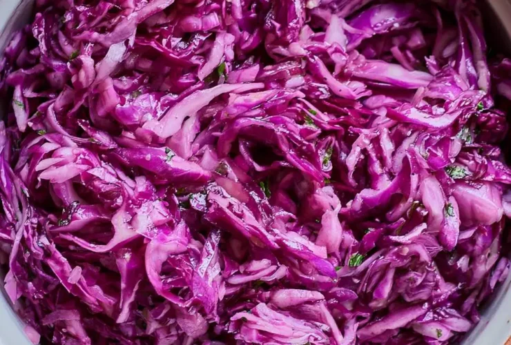 A bowl of vibrant purple cabbage recipe salad with fresh herbs and light dressing on a wooden surface.