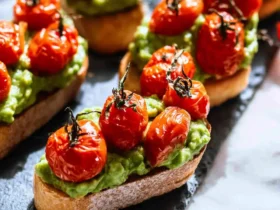 Roasted Tomato Crostini with Avocado 44 Roasted Tomato Crostini with Avocado arranged on a slate serving board, featuring toasted bread topped with mashed avocado and blistered cherry tomatoes.