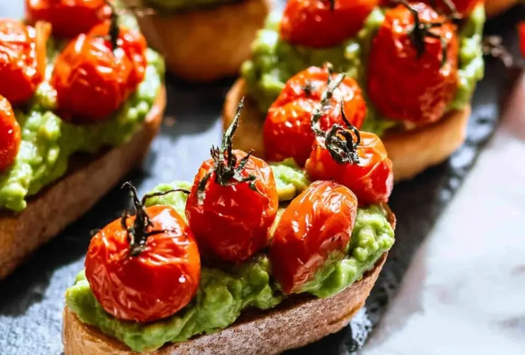 Roasted Tomato Crostini with Avocado arranged on a slate serving board, featuring toasted bread topped with mashed avocado and blistered cherry tomatoes.