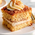 A slice of Sour Cream Coffee Cake with creamy filling, crumb topping, and swirled frosting on a white plate.