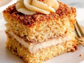 Sour Cream Coffee Cake 47 A slice of Sour Cream Coffee Cake with creamy filling, crumb topping, and swirled frosting on a white plate.