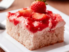 Strawberry Sheet Cake 41 A slice of strawberry sheet cake topped with fresh strawberries and glossy strawberry glaze on a white plate.