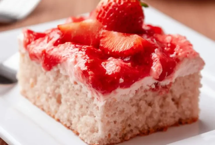 A slice of strawberry sheet cake topped with fresh strawberries and glossy strawberry glaze on a white plate.