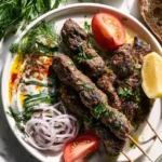 Grilled Turkish Beef Kofta Recipe served on a plate with yogurt sauce, fresh vegetables, and herbs.